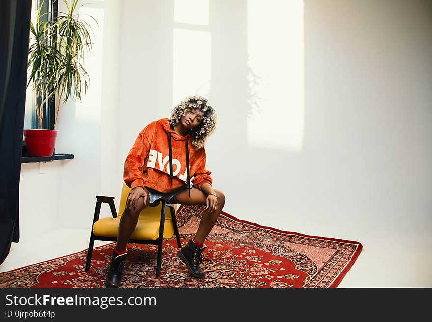 Woman Wearing Orange Pullover Hoodie Sitting on Chair&#x27;s Arm