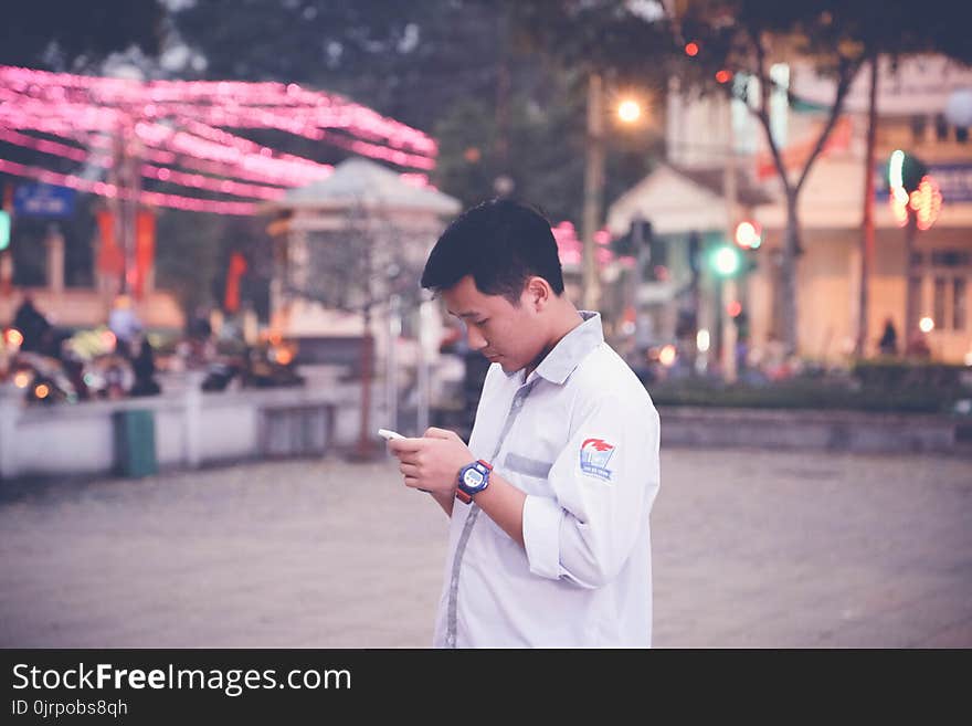 Focus Photography of Man Wearing White Sports Shirt Holding Smartphone Near Buntings