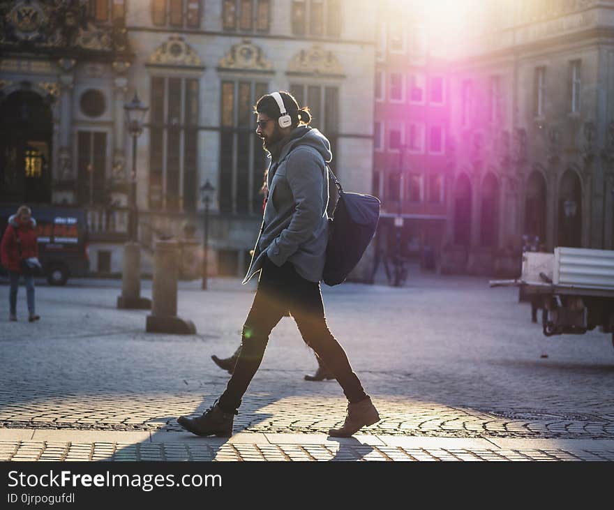 Man in Gray Hooded Jacket Walking on Gray Bricks Pavement