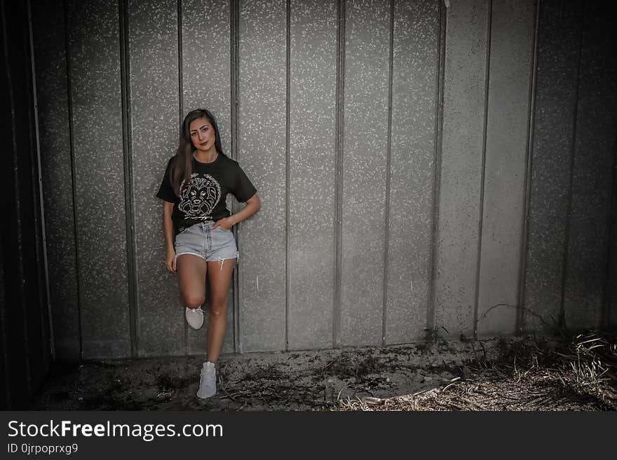 Woman Wearing Black Shirt and Daisy Dukes Leaning on Wall