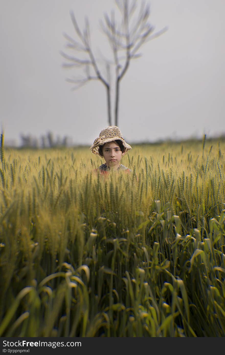 Toddler Wearing Brown Hat in the Middle of Green Field