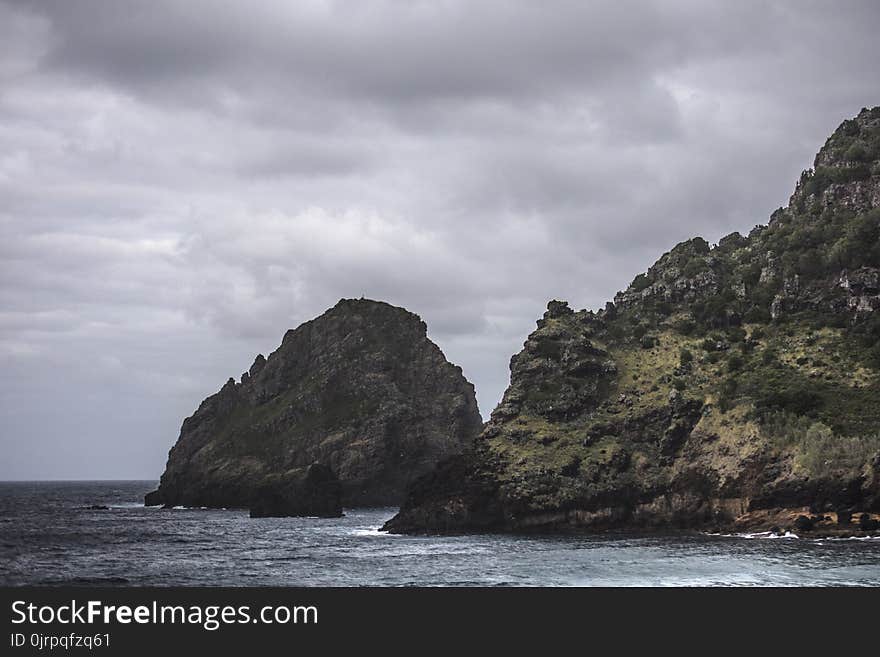 Brown Rock Formation on Body of Water Under Gray Clouds