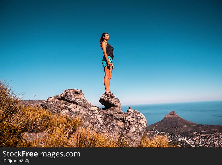 Woman in Black Top and Blue Shorts on Stone Under Blue Sky