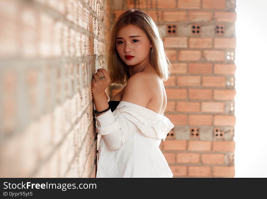 Shallow Focus Photography of Woman in White Top Beside Red Brick Wall