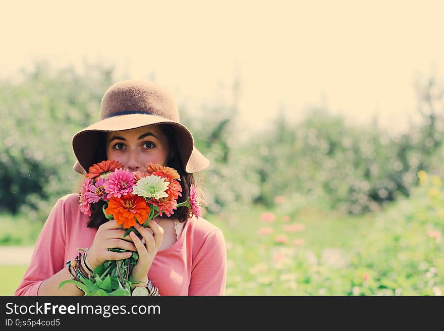 Woman Wearing Hat and Holding Flowers Surrounded by Plants