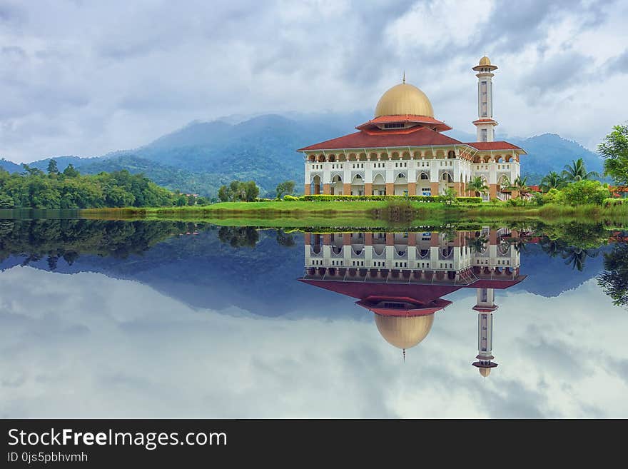 White and Red House Reflecting on Body of Water Under Blue Sky