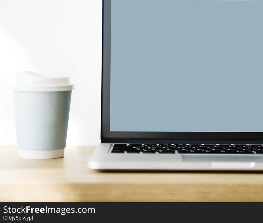 Macbook Pro Beside Gray Disposable Cup on Brown Wooden Surface