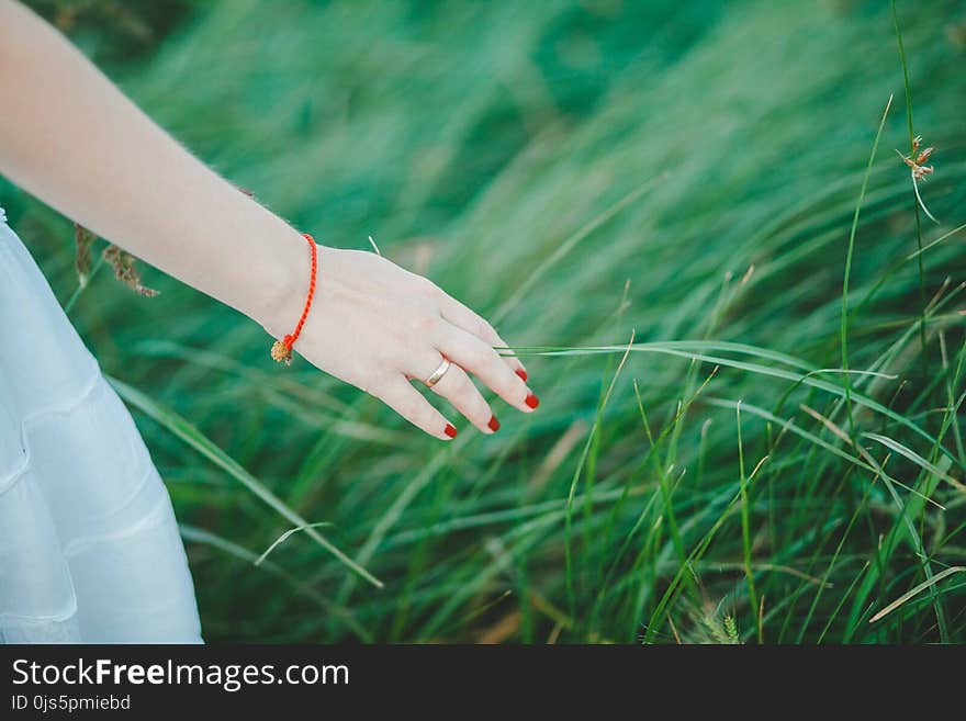 Woman Wearing White Skirt, Orange Bracelet, and Red Manicure Beside Green Grass