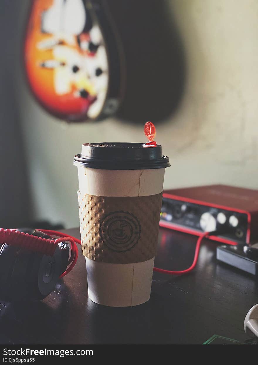 White and Brown Labeled Plastic Coffee Cup on Brown Tabletop Near Black Multimedia Player