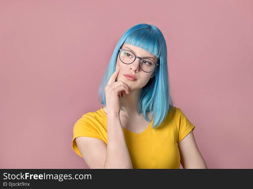 Beautiful pensive young woman with blue color dyed hair with hipster style spectacles thinking in front of pastel studio background. Beautiful pensive young woman with blue color dyed hair with hipster style spectacles thinking in front of pastel studio background.