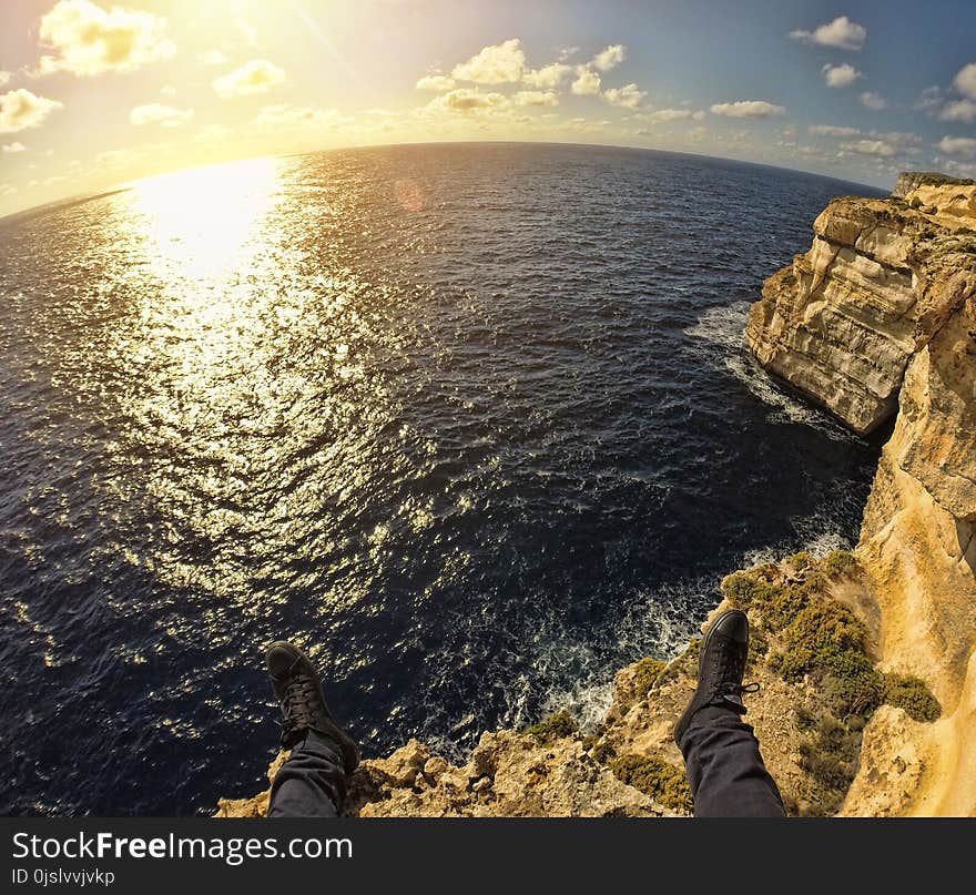 Person on Top of Stone Island in Front of Sea during Sunset