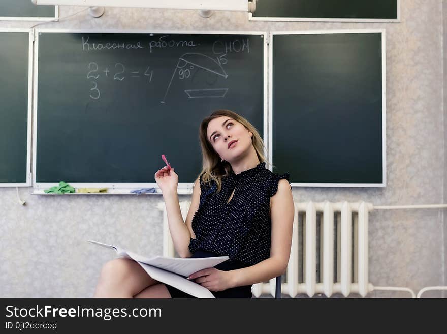 Strict young blonde teacher sits on a chair crossing her legs and dreamy looks at the ceiling