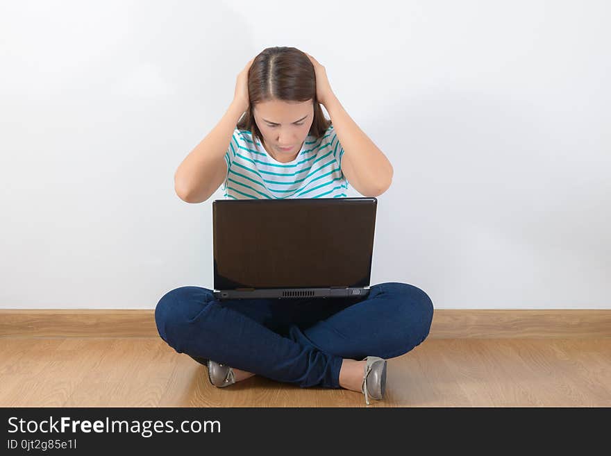 Tired teen woman with laptop sitting on the wooden floor