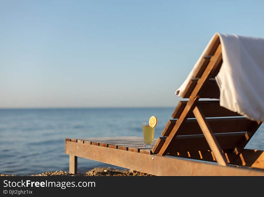 White polo shirt and glass of cold drink on sunbed at pebble sea beach at dawn. Horizontal image with copyspace. White polo shirt and glass of cold drink on sunbed at pebble sea beach at dawn. Horizontal image with copyspace