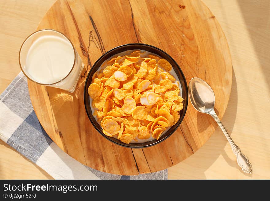 Cornflakes breakfast cereal in the bowl with glass of milk on wood table