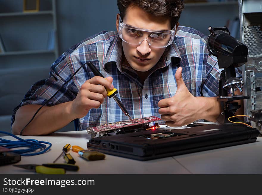 Young repair technician soldering electrical parts on motherboar