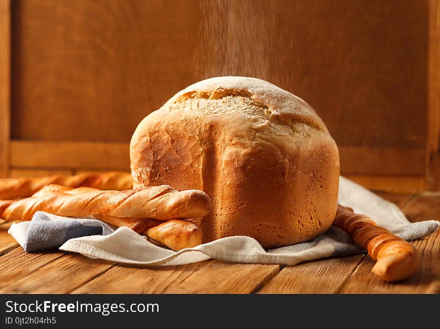 Flour is pouring on loaf and four french baguettes. Bread lay on napkin on rustic wooden table. Concept of homemade pastry or bakery. Flour is pouring on loaf and four french baguettes. Bread lay on napkin on rustic wooden table. Concept of homemade pastry or bakery