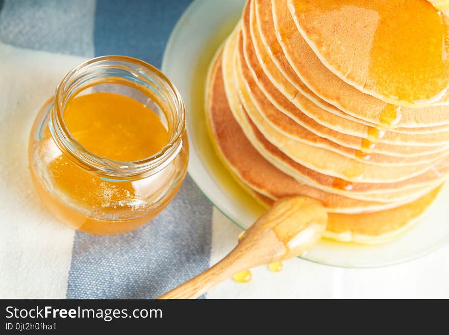 Stack of pancakes with pouring honey on plate with wooden spoon and jar with honey. Concept of tasty breakfast, close-up view. Selective focus. Stack of pancakes with pouring honey on plate with wooden spoon and jar with honey. Concept of tasty breakfast, close-up view. Selective focus