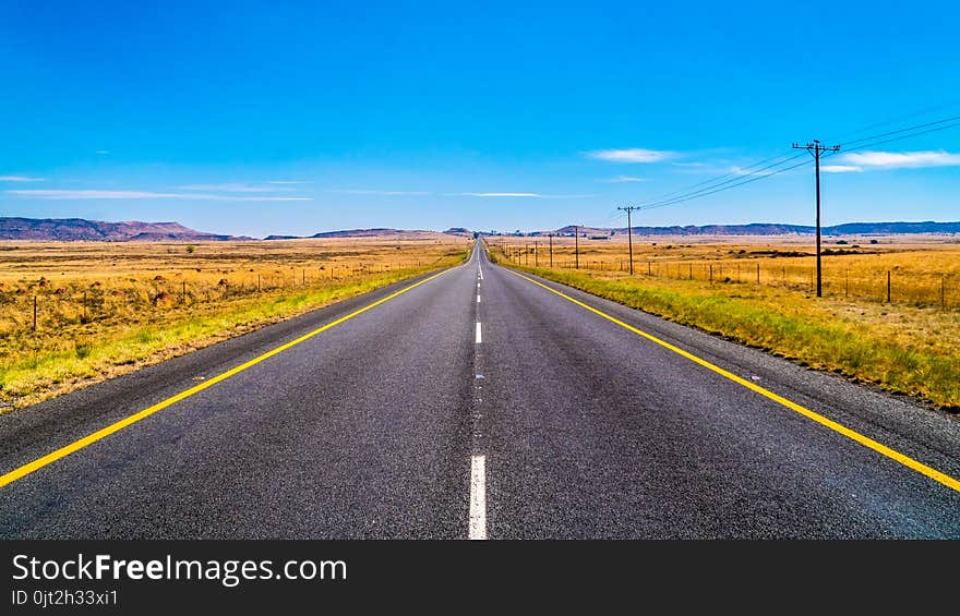 Long Straight Road through the Endless wide open landscape of the semi desert Karoo Region in Free State and Eastern Cape provinces in South Africa under blue sky