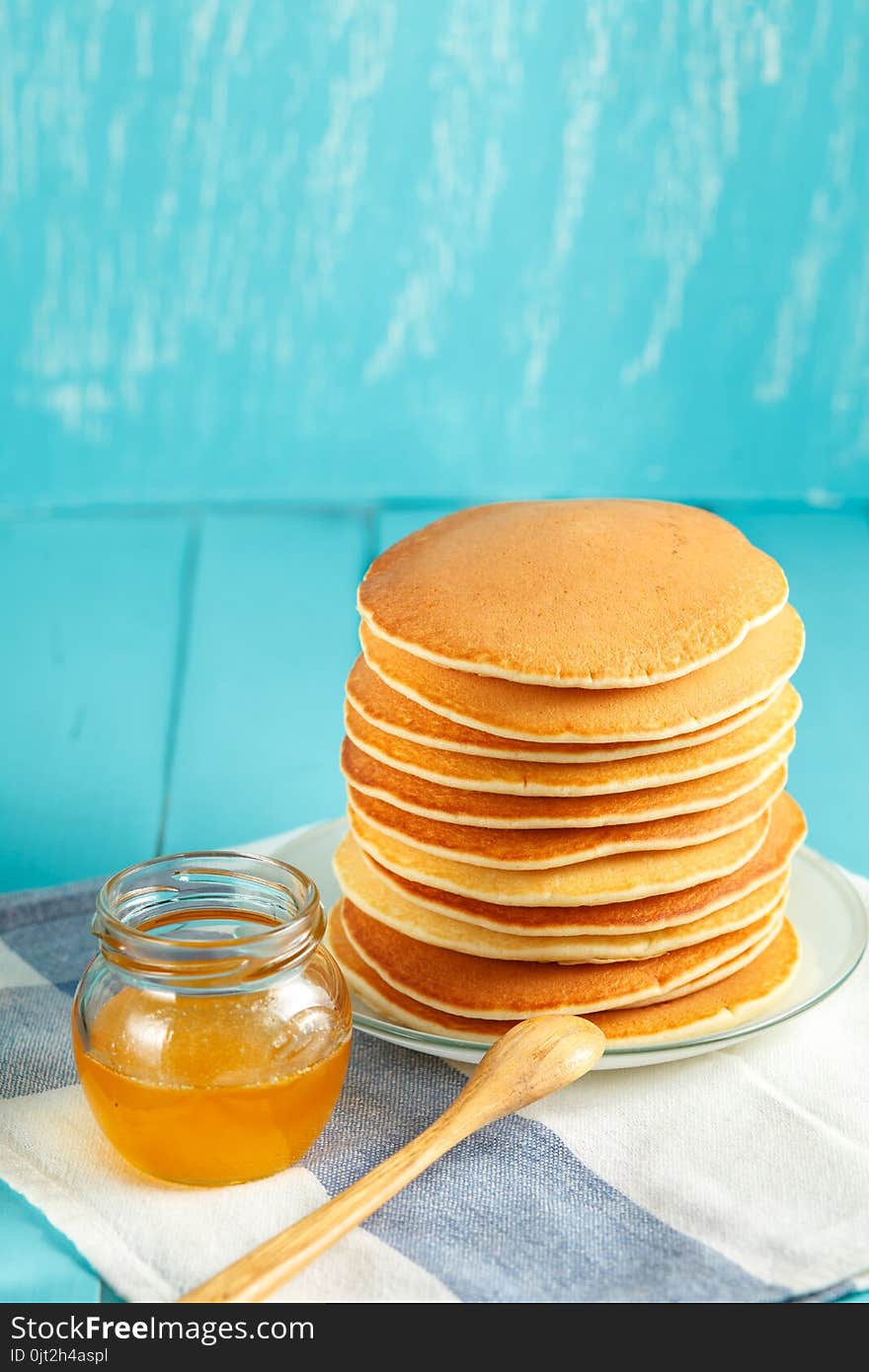 Stack of pancakes with honey and piece of butter on plate with wooden spoon and jar with honey. Copyspace. Concept of shrovetide treats or tasty food. Selective focus. Stack of pancakes with honey and piece of butter on plate with wooden spoon and jar with honey. Copyspace. Concept of shrovetide treats or tasty food. Selective focus