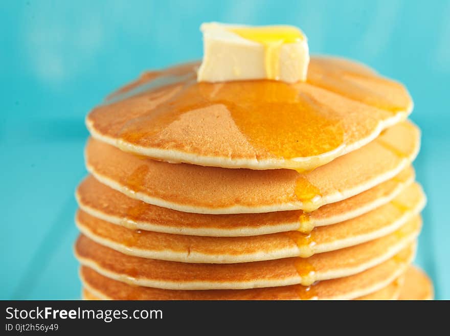 Stack of pancakes with honey and piece of butter on plate which stands on napkin on blue wooden table. Copyspace. Concept of shrovetide treats. Selective focus. Stack of pancakes with honey and piece of butter on plate which stands on napkin on blue wooden table. Copyspace. Concept of shrovetide treats. Selective focus