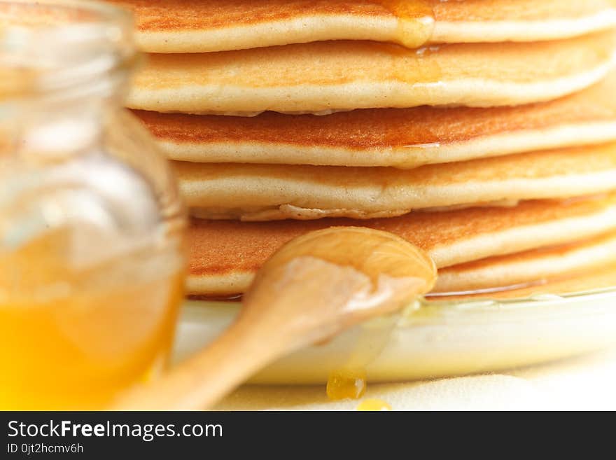 Close up of stack of pancake with pouring honey, wooden spoon and jar of honey