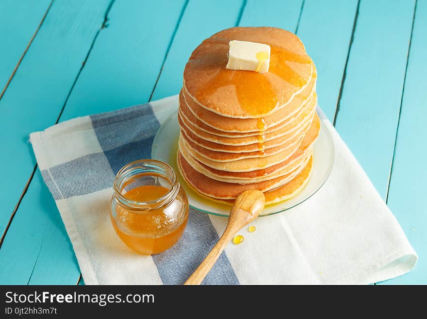 Stack of pancakes with pouring honey on plate with wooden spoon and jar with honey. Concept of tasty breakfast, close-up view. Selective focus. Stack of pancakes with pouring honey on plate with wooden spoon and jar with honey. Concept of tasty breakfast, close-up view. Selective focus