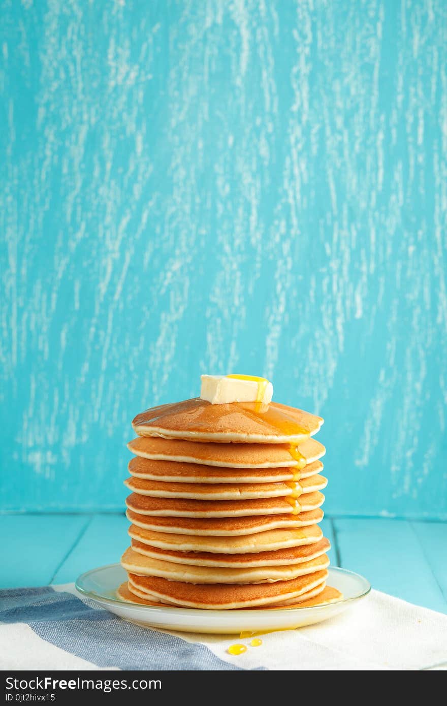 Stack of pancakes with honey and piece of butter on plate which stands on napkin on blue wooden table. Copyspace. Concept of shrovetide treats or tasty food. Selective focus. Stack of pancakes with honey and piece of butter on plate which stands on napkin on blue wooden table. Copyspace. Concept of shrovetide treats or tasty food. Selective focus