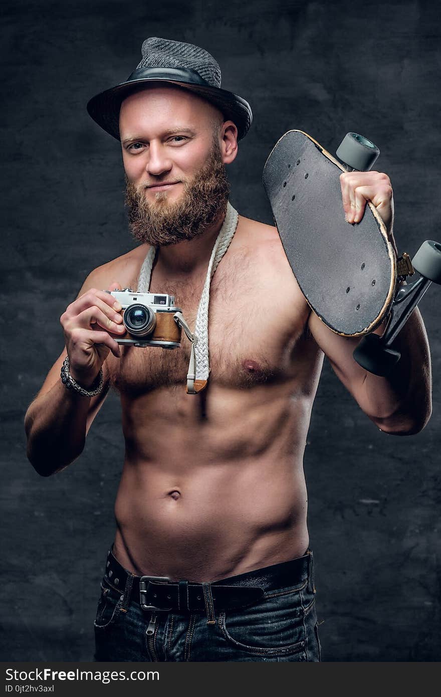 The shirtless bearded male holds skateboard.