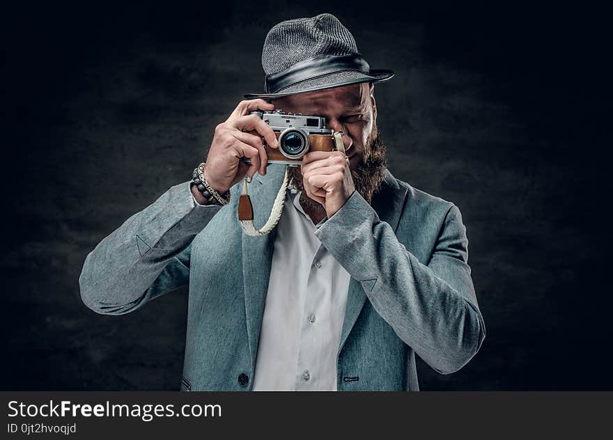 A man dressed in a grey jacket and felt hat holds an SLR photo c