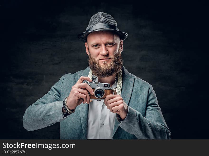 A man dressed in a grey jacket and felt hat holds an SLR photo c