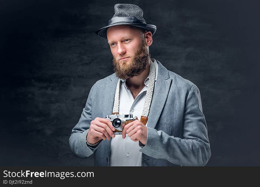 Studio portrait of bearded photographer dressed a suit and felt hat holds an old vintage SLR photo camera. Studio portrait of bearded photographer dressed a suit and felt hat holds an old vintage SLR photo camera.