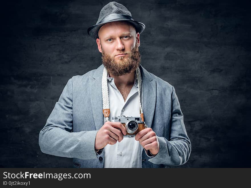 Studio portrait of bearded photographer dressed a suit and felt hat holds an old vintage SLR photo camera. Studio portrait of bearded photographer dressed a suit and felt hat holds an old vintage SLR photo camera.