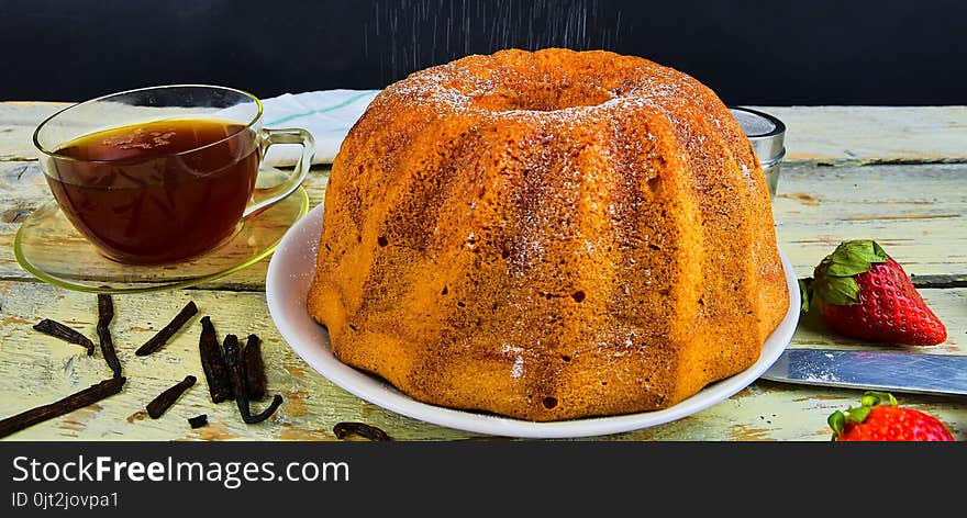 Old fashioned sand cake with cup of black tea and pieces of vanilla on wooden background. Egg-yolk sponge cake on rustic white background. Pouring sugar on sand cake.