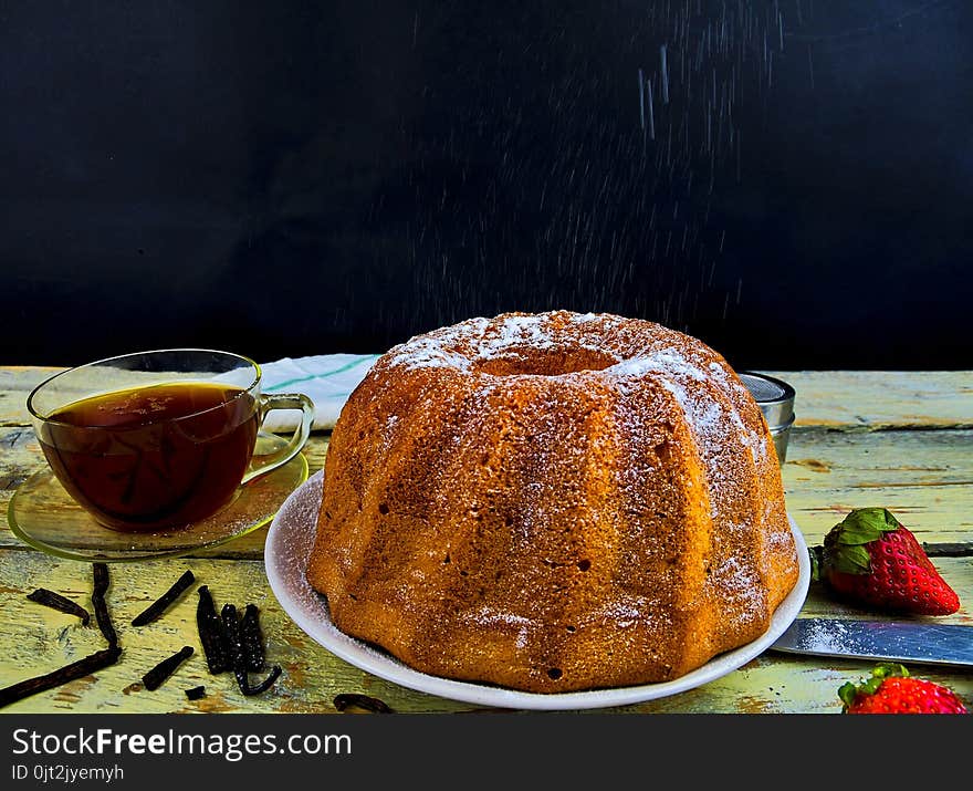 Old fashioned sand cake with cup of black tea and pieces of vanilla on wooden background. Egg-yolk sponge cake on rustic white background. Pouring sugar on sand cake.