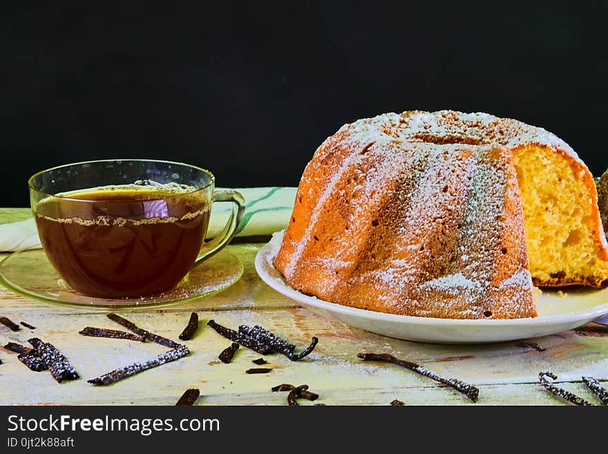 Old fashioned sand cake with cup of black tea and pieces of vanilla on wooden background. Egg-yolk sponge cake on rustic white background