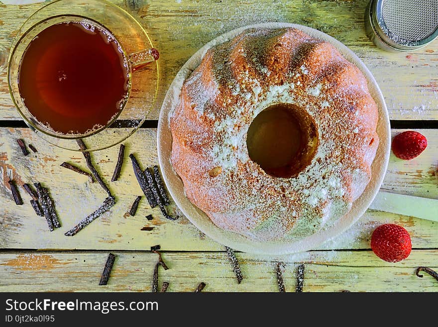 Old fashioned sand cake with cup of black tea and pieces of vanilla on wooden background. Egg-yolk sponge cake with stawberries on rustic white background. Top view. Flat design.