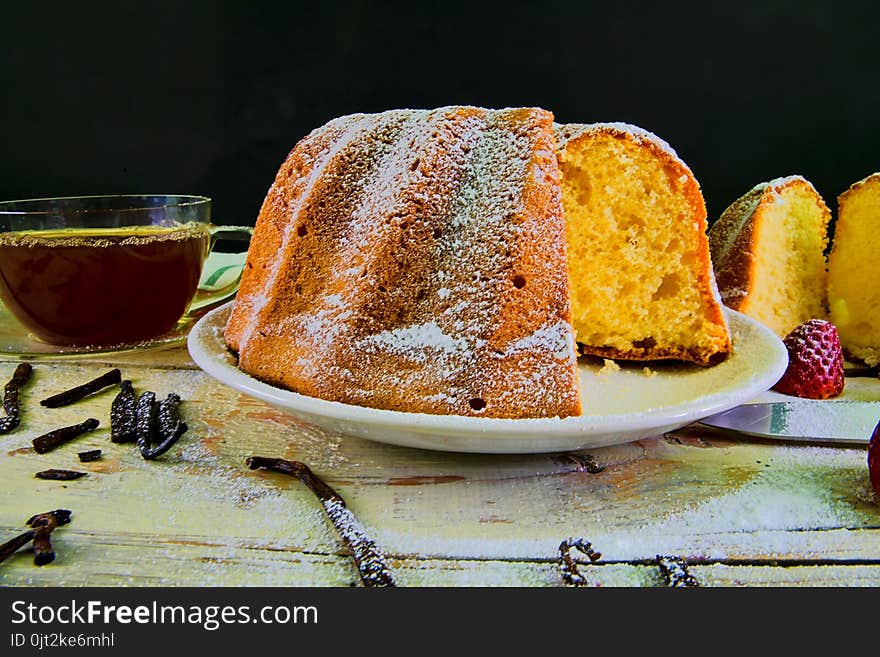 Old fashioned sand cake with cup of black tea and pieces of vanilla on wooden background. Egg-yolk sponge cake with stawberries on rustic white background