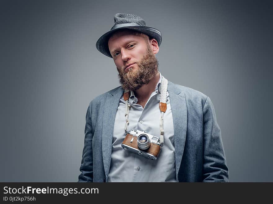 Studio portrait of bearded photographer dressed a suit and felt hat holds an old vintage SLR photo camera. Studio portrait of bearded photographer dressed a suit and felt hat holds an old vintage SLR photo camera.