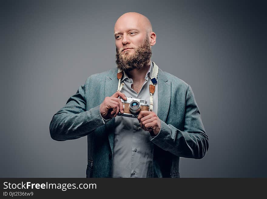 A stylish bearded hipster male dressed in a grey jacket and felt hat holds an SLR photo camera. A stylish bearded hipster male dressed in a grey jacket and felt hat holds an SLR photo camera.