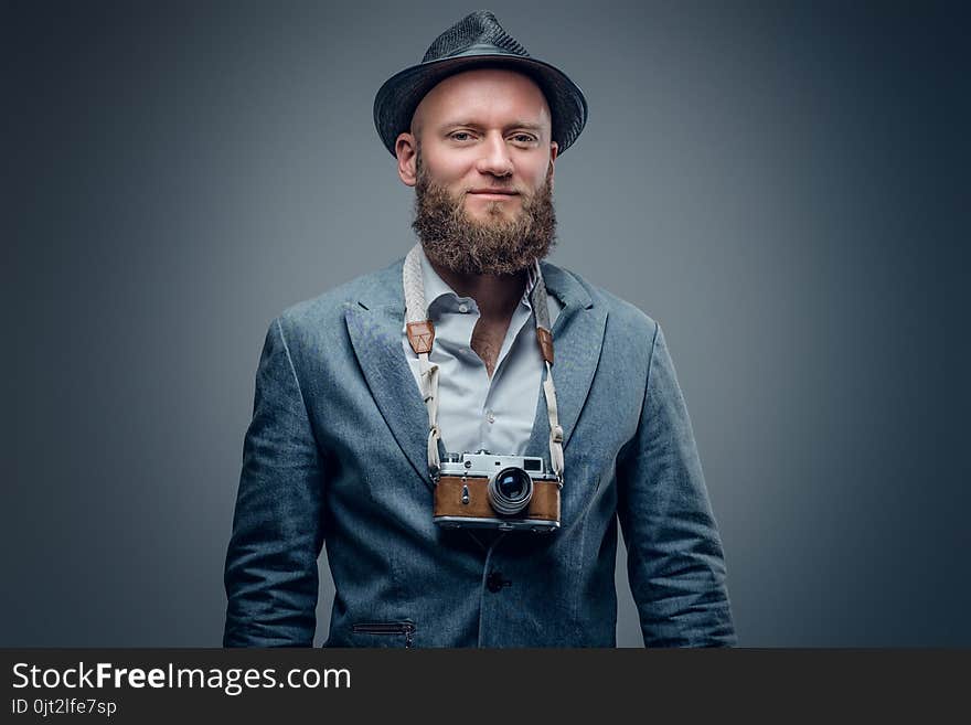 Studio portrait of bearded photographer dressed a suit and felt hat holds an old vintage SLR photo camera. Studio portrait of bearded photographer dressed a suit and felt hat holds an old vintage SLR photo camera.