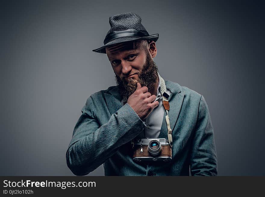 A man dressed in a grey jacket and felt hat holds an SLR photo c