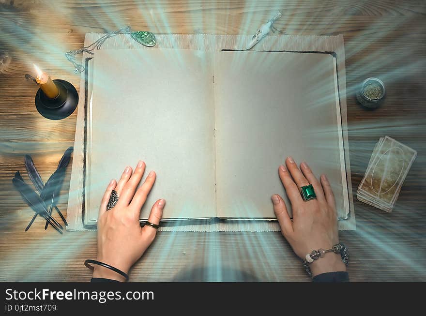 Book of magic with mystical light and copy space. Tarot cards on fortune teller desk table. Future reading. Woman witch reads a ancient magic scroll book and learn art of prediction on wooden table. Book of magic with mystical light and copy space. Tarot cards on fortune teller desk table. Future reading. Woman witch reads a ancient magic scroll book and learn art of prediction on wooden table.