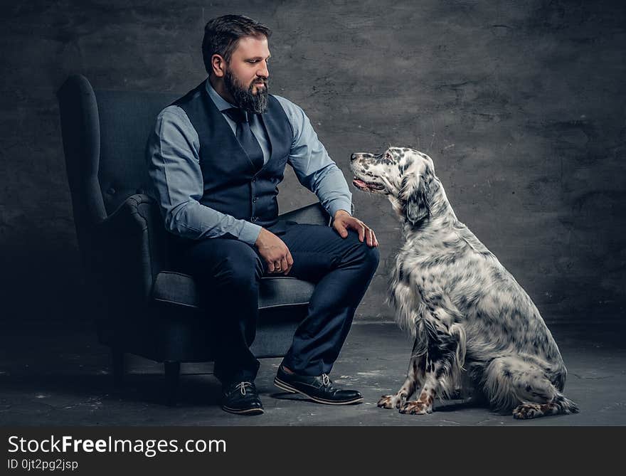 Portrait of stylish bearded male sits on a chair and the Irish setter dog.