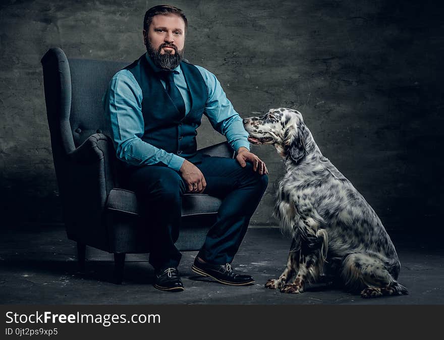 Portrait of stylish bearded male sits on a chair and the Irish setter dog.