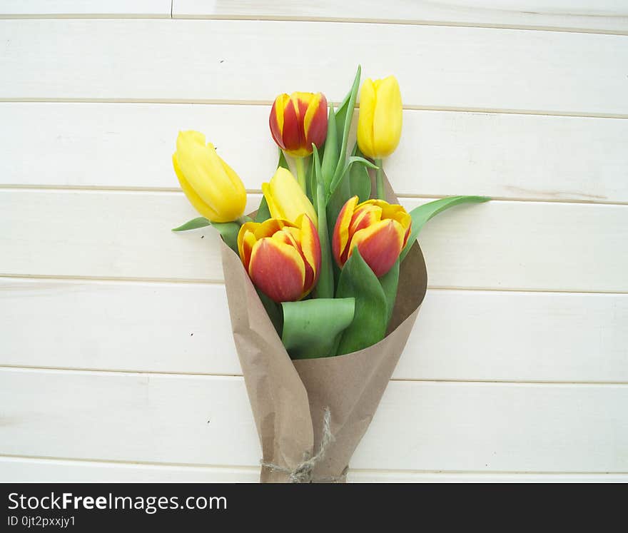 Spring bouquet for mom. View from above. The child gives a gift. A bouquet of yellow, red and orange tulips in a crafted package. Valentine`s Day. Wooden background. Mother`s Day and March 8th.