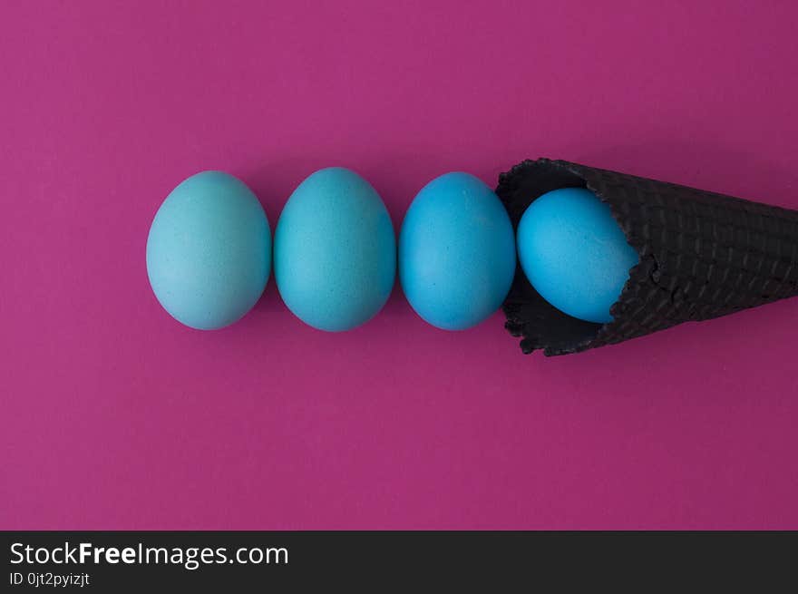 Easter. Blue eggs are poured from a waffle cone from ice cream. Black waffle cone. Ice cream egg. Pink background. Conceptual photo.