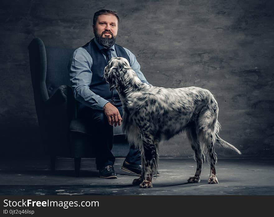 Stylish bearded male sits on a chair and the Irish setter dog.