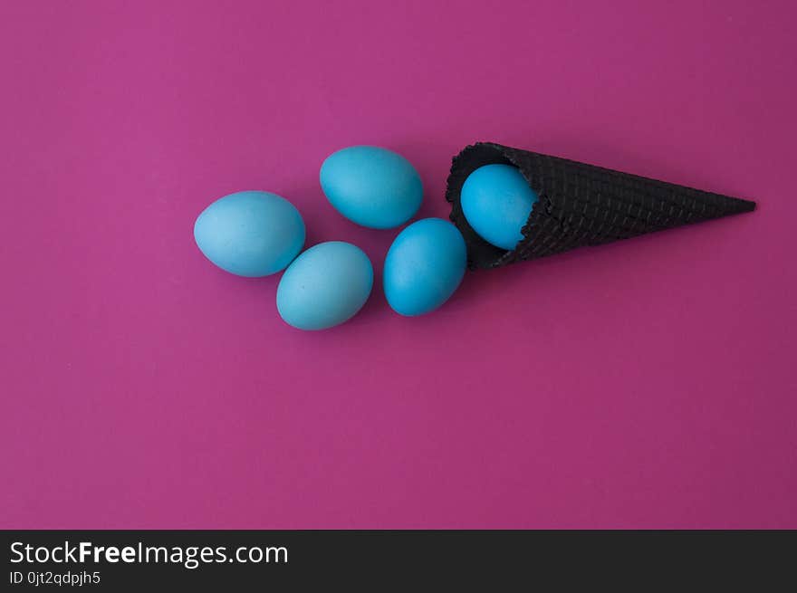 Easter. Blue eggs are poured from a waffle cone from ice cream. Black waffle cone. Ice cream egg. Pink background. Conceptual photo.