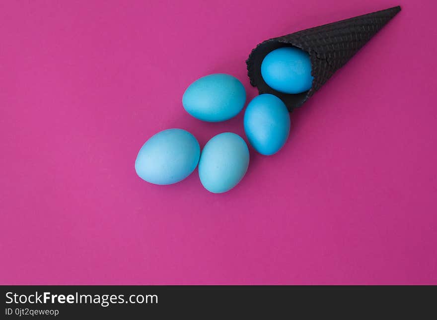 Easter. Blue eggs are poured from a waffle cone from ice cream. Black waffle cone. Ice cream egg. Pink background. Conceptual photo.